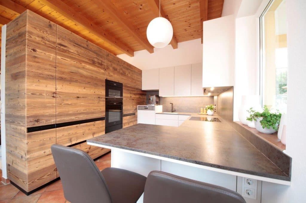 Moderne Küche mit Holzdecke, weißen Schränken und dunkler Arbeitsplatte neben einem großen Fenster