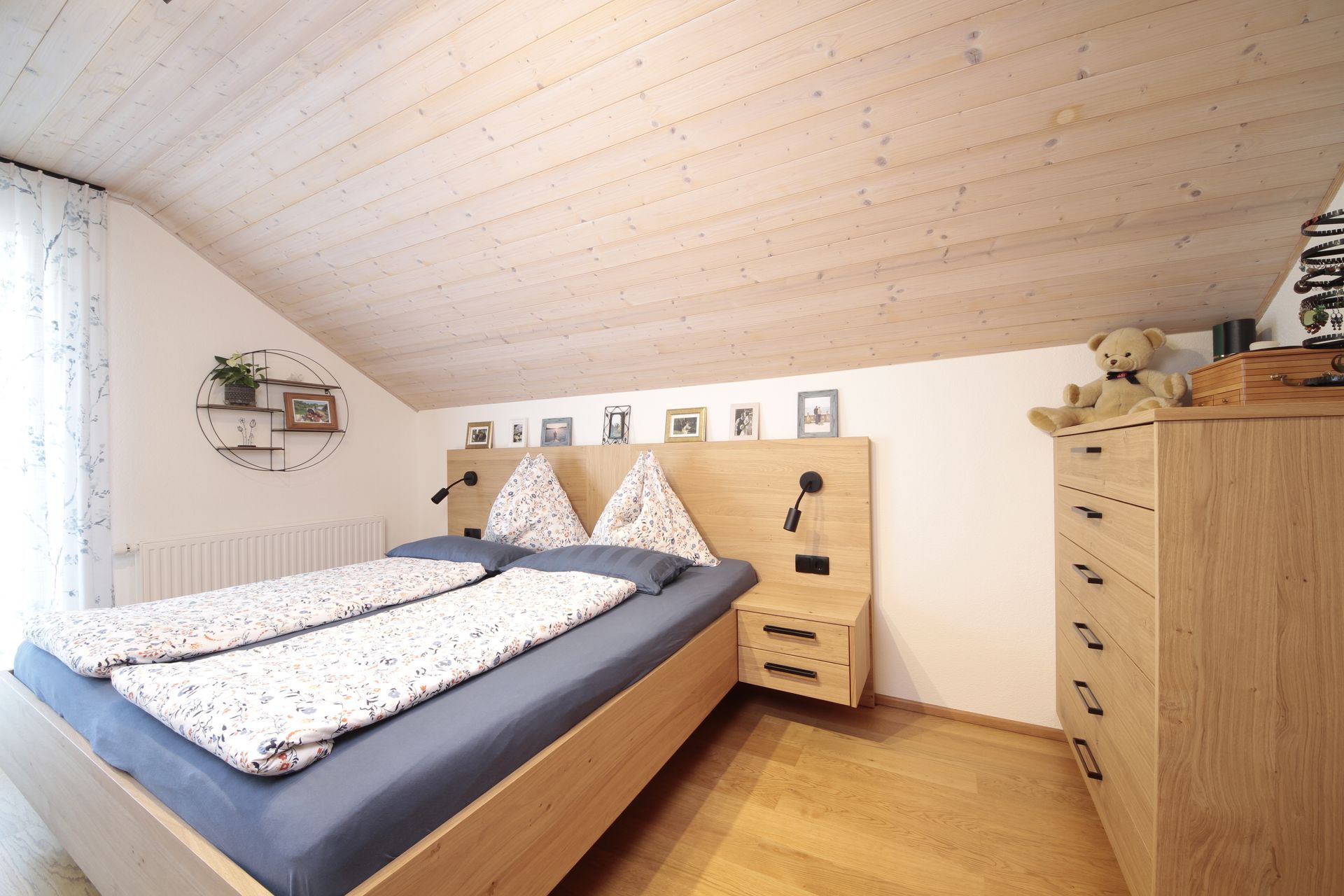 Gemütliches Dachgeschosszimmer mit Bett, Holzkommode und schräger weißer Decke.