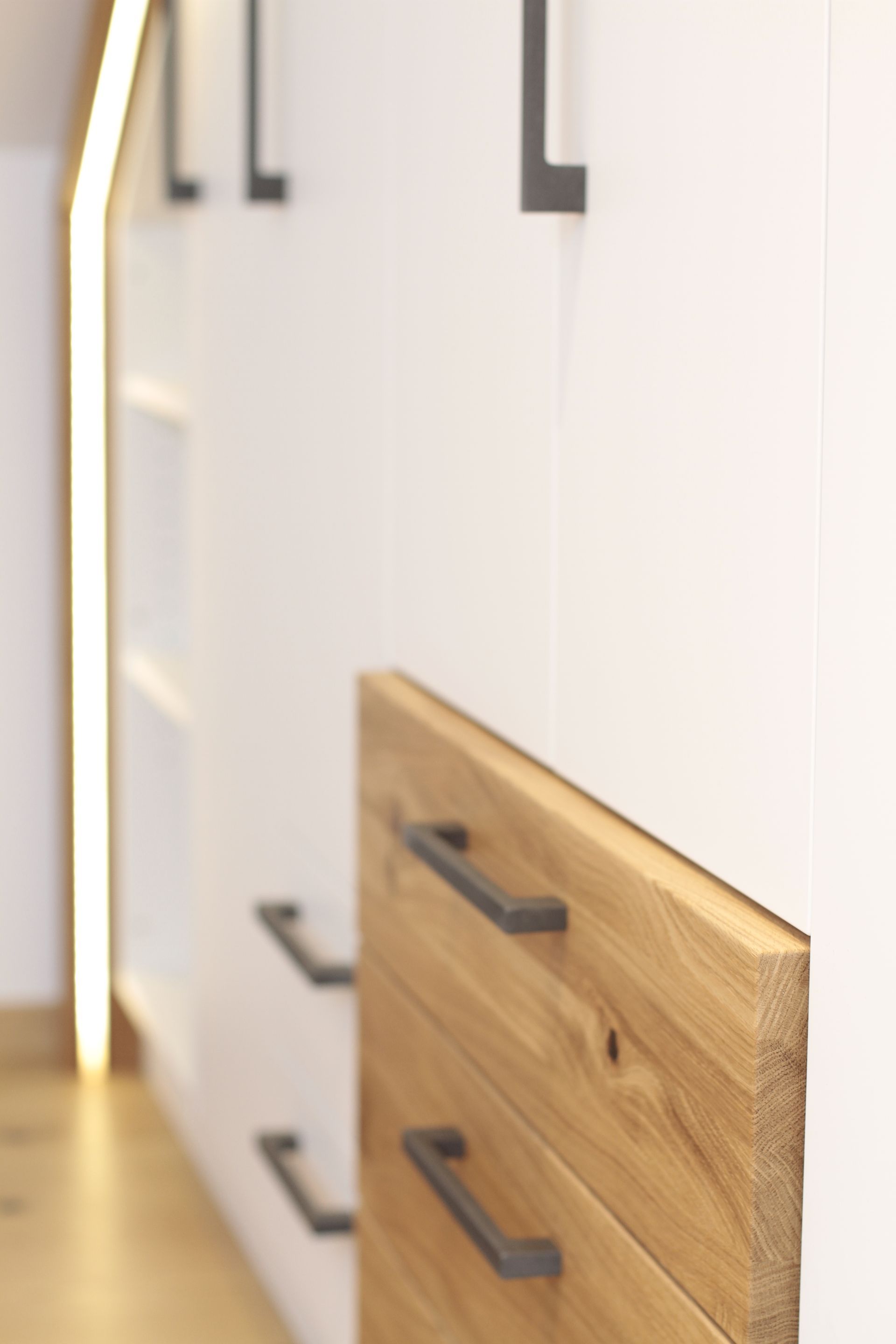 Moderne Küchenschubladen mit schwarzen Griffen, darunter eine teilweise zu öffnende Schublade mit Holzfront.