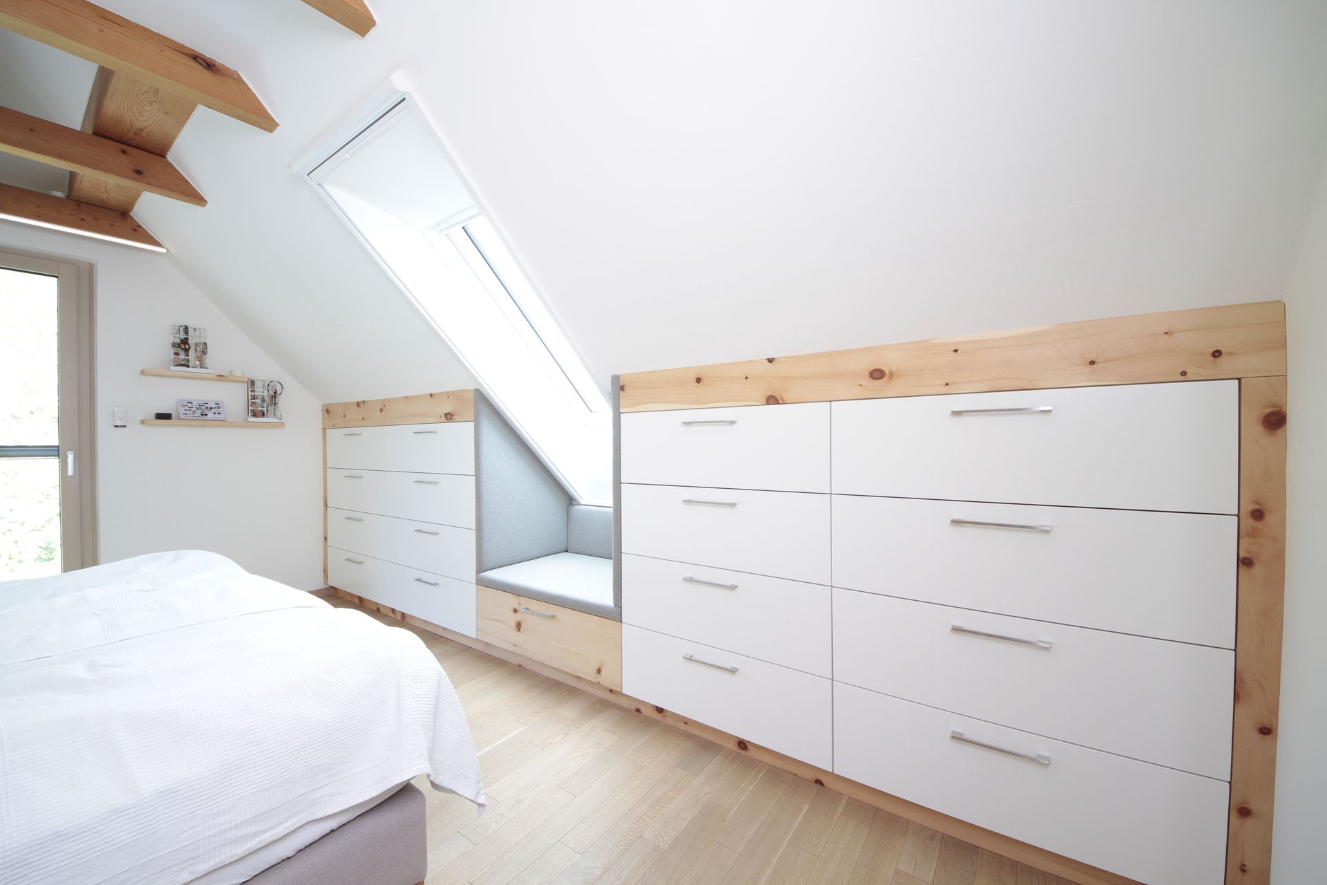 Helles Dachgeschoss-Schlafzimmer mit weißen Aufbewahrungsschubladen, Dachfenster und hellen Holzelementen