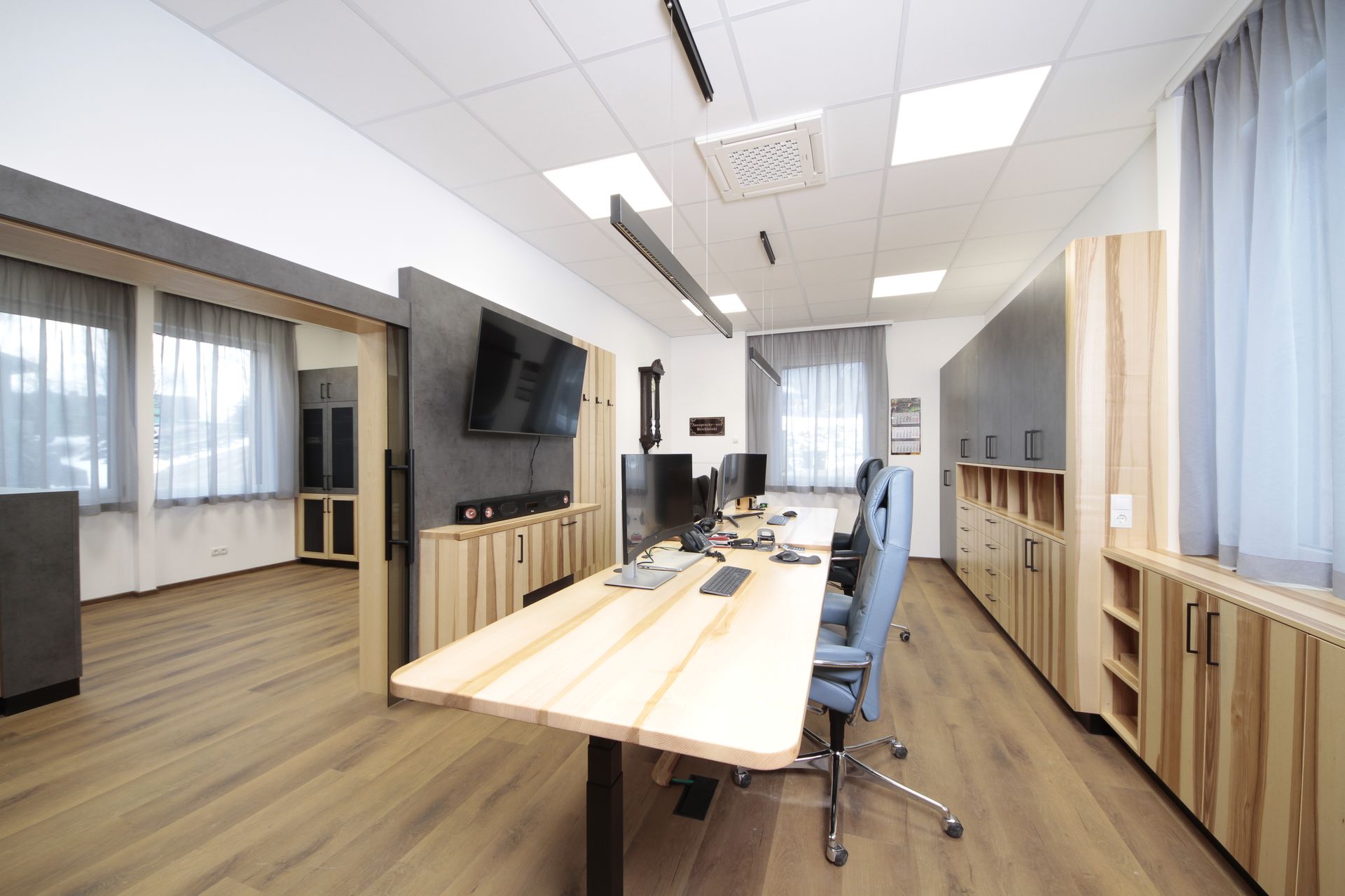 Moderner Bürokonferenzraum mit langen Holztischen, blauen Stühlen, Wandfernseher und großen Fenstern