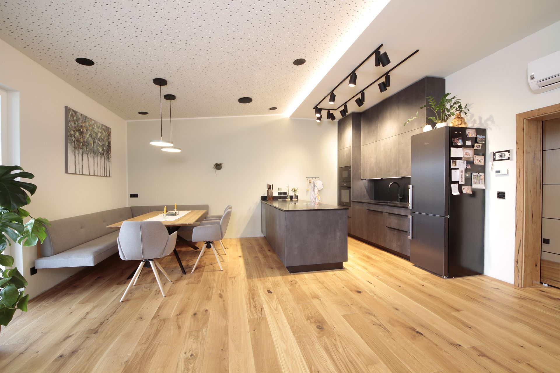 Helles, modernes offenes Wohnzimmer mit Küche, Holzböden, Esstisch, grauem Sofa und schwarzen Schränken.