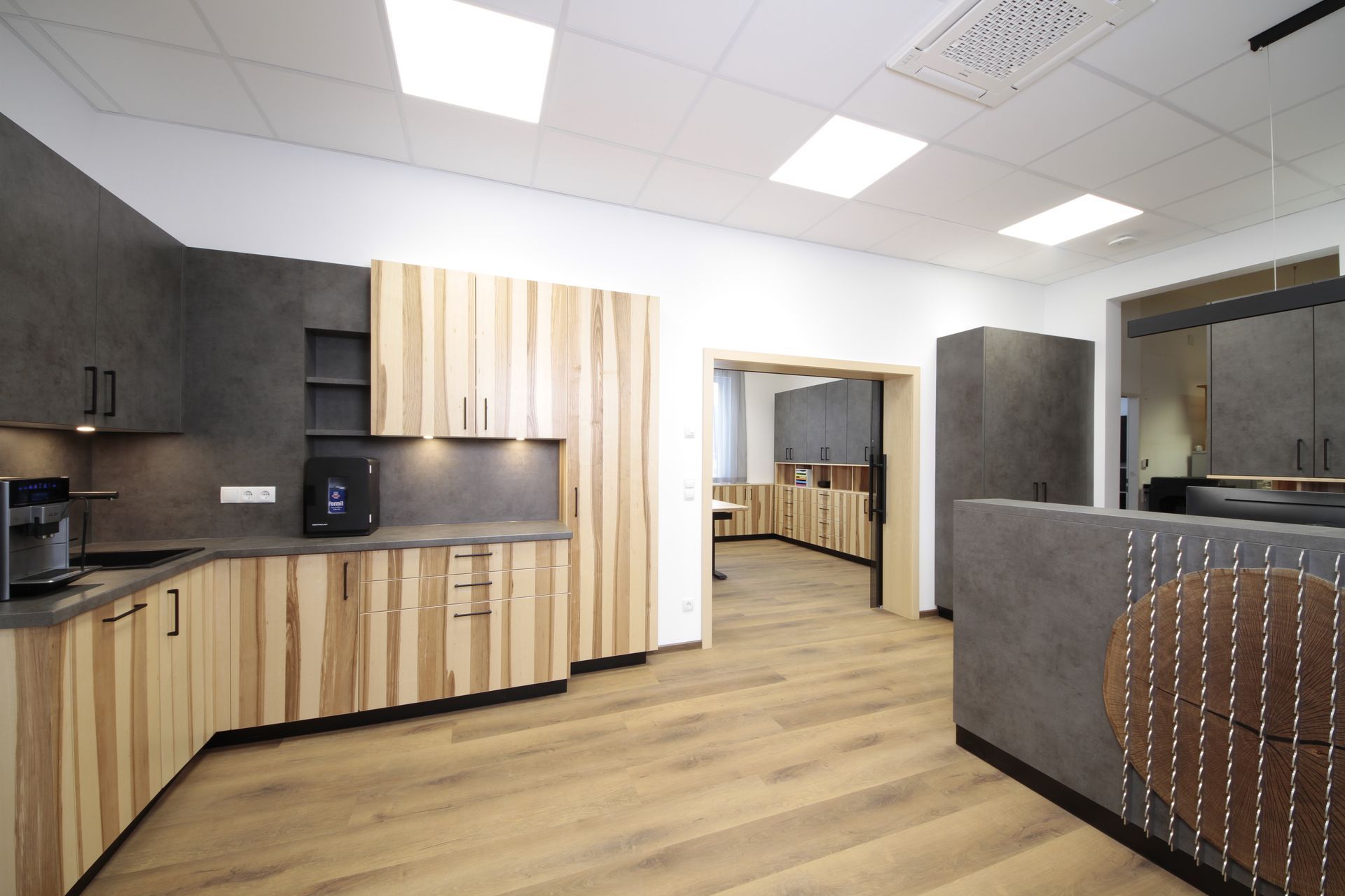 Moderne Küche mit Holzschränken, weißen Deckenleuchten und einem zentralen Durchgang zu einem anderen Raum