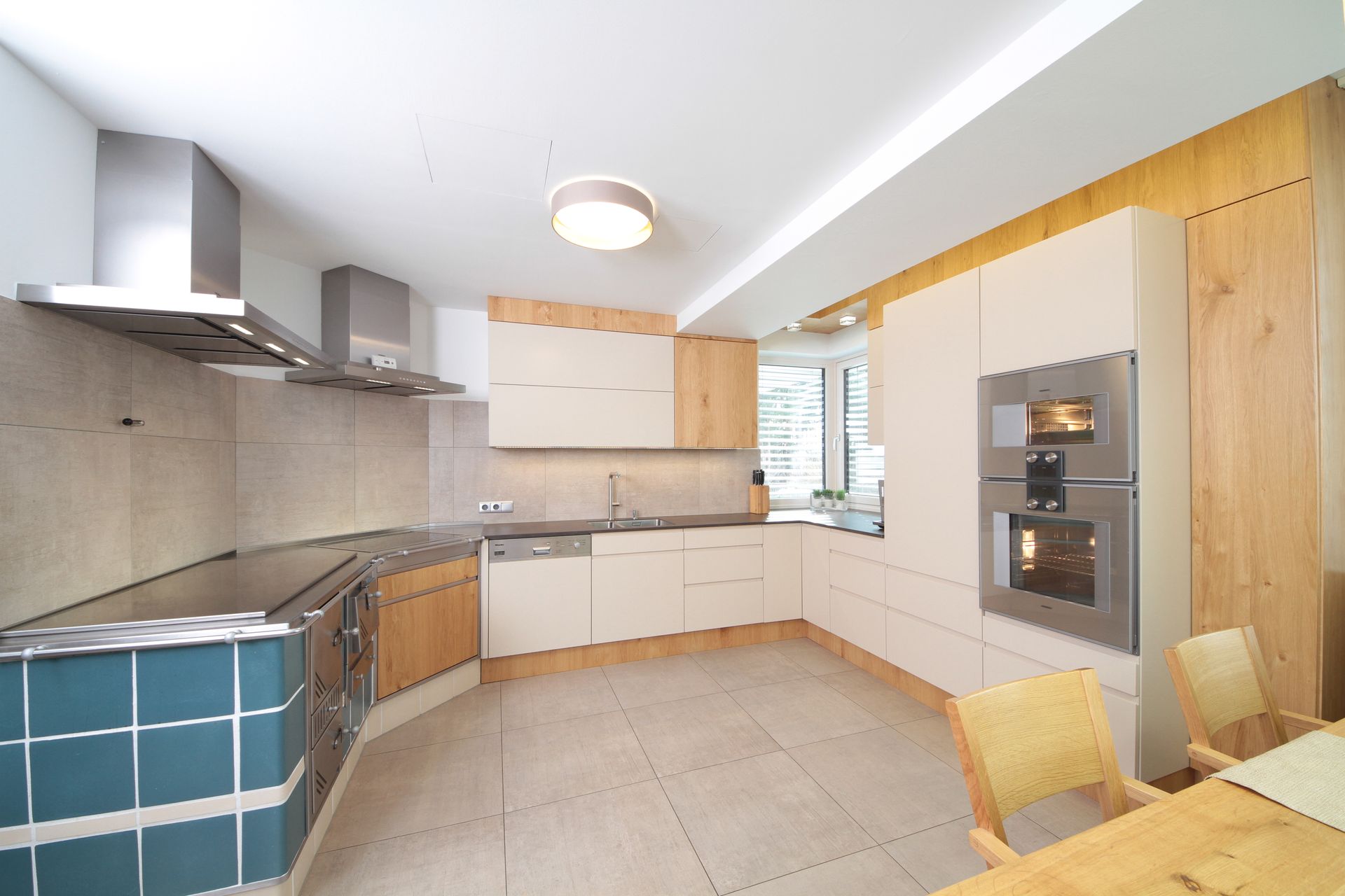 Moderne Küche mit hellen Holzschränken, grauen Arbeitsplatten, Fliesenboden und eingebautem Backofen.