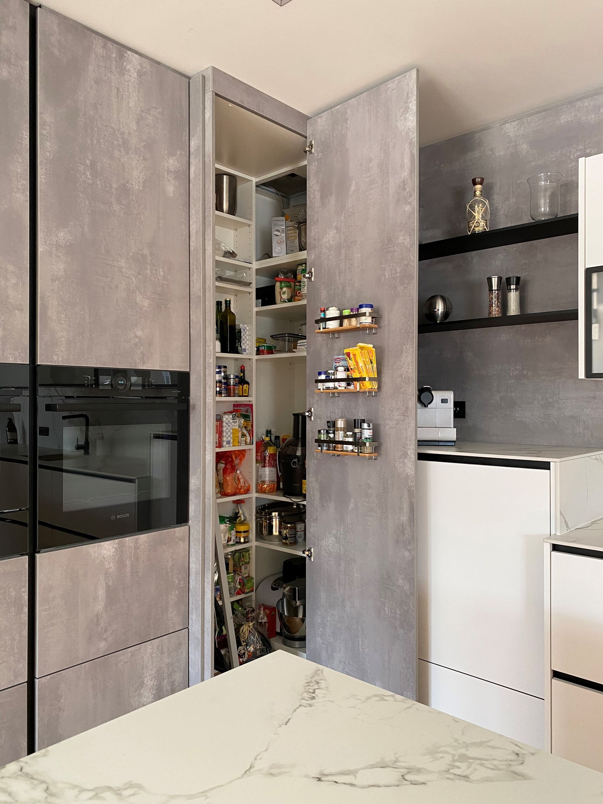 Moderne Küche mit hohen grauen Schränken, offener Speisekammer und weißer Kücheninsel.