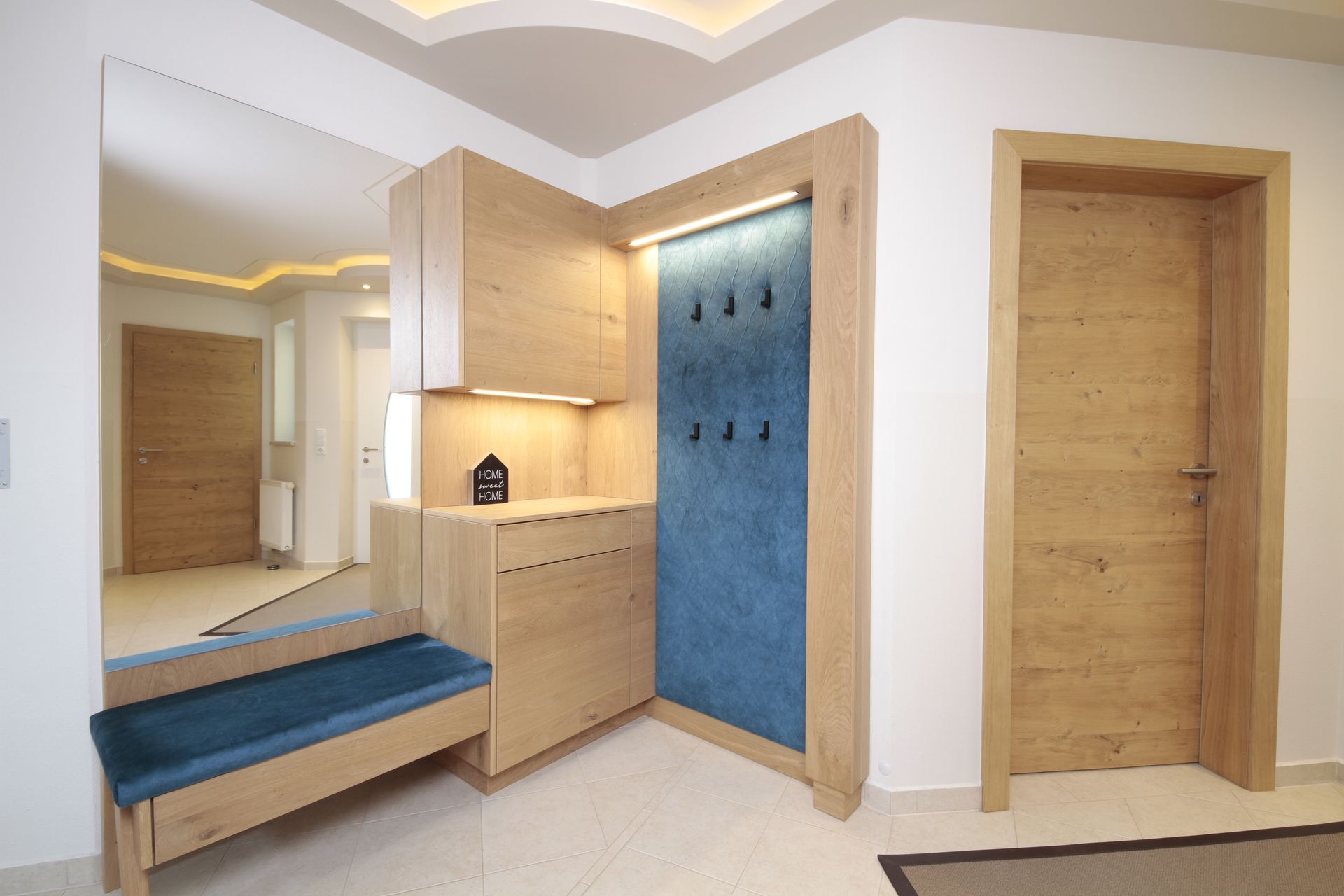 Moderner Eingangsbereich mit blauer Bank, Spiegel, Holzschränken und zwei Holztüren in einem hellen Interieur