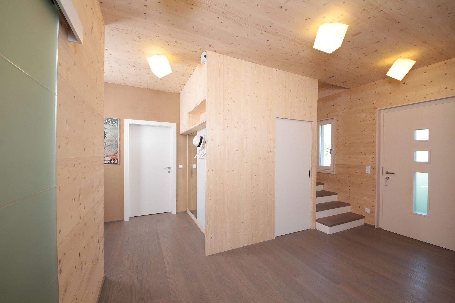 Heller, holzgetäfelter Flur mit Treppe, weißen Türen und Deckenleuchten