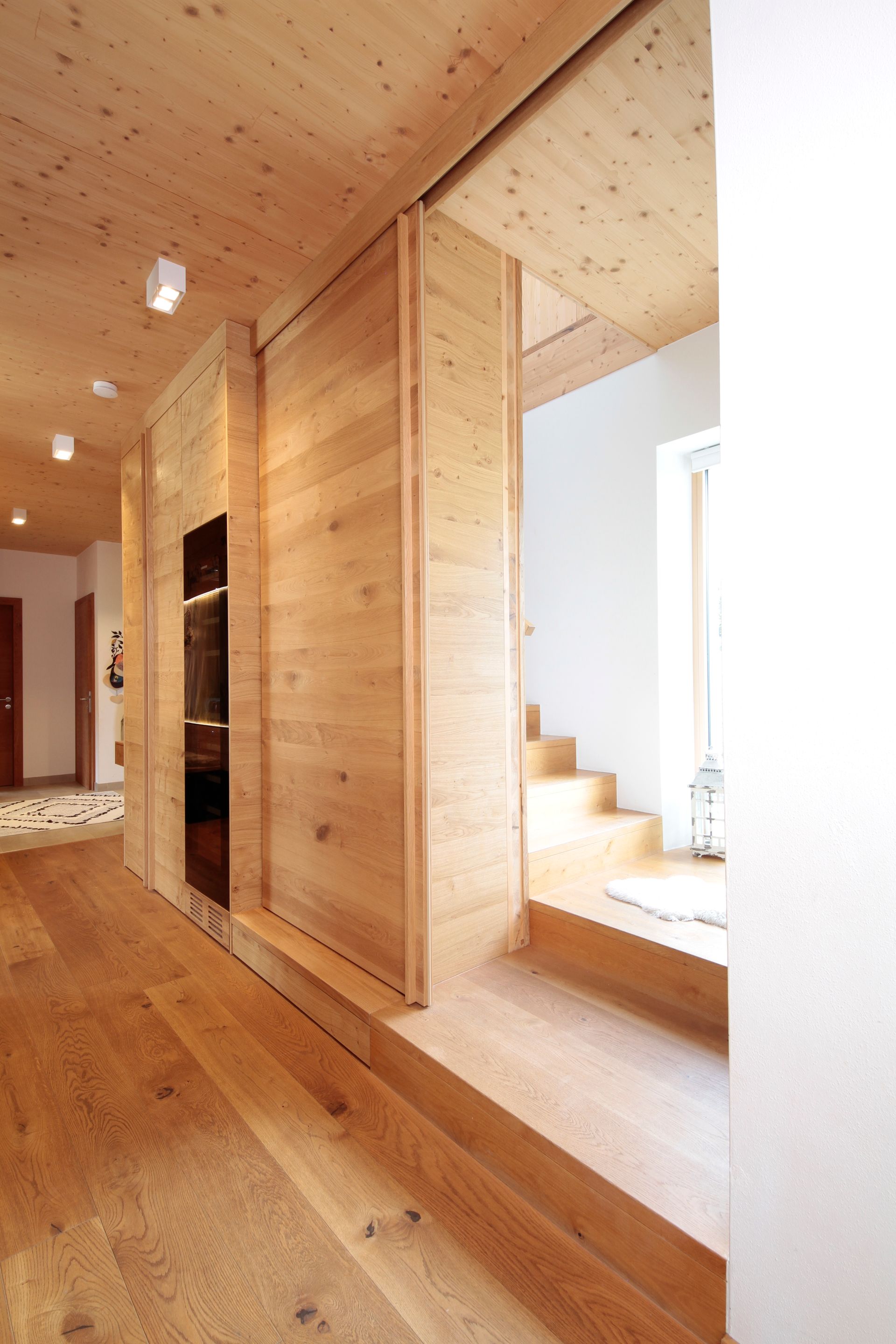 Holzflur mit Einbauschränken und einem von einem hellen Fenster beleuchteten Treppenhaus.