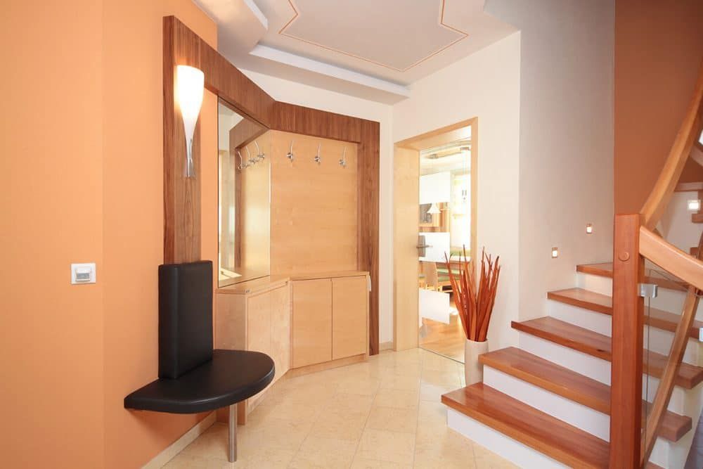 Helles Foyer mit Holztreppe, Einbauschränken und einem kleinen schwarzen Tisch vor pfirsichfarbenen Wänden.