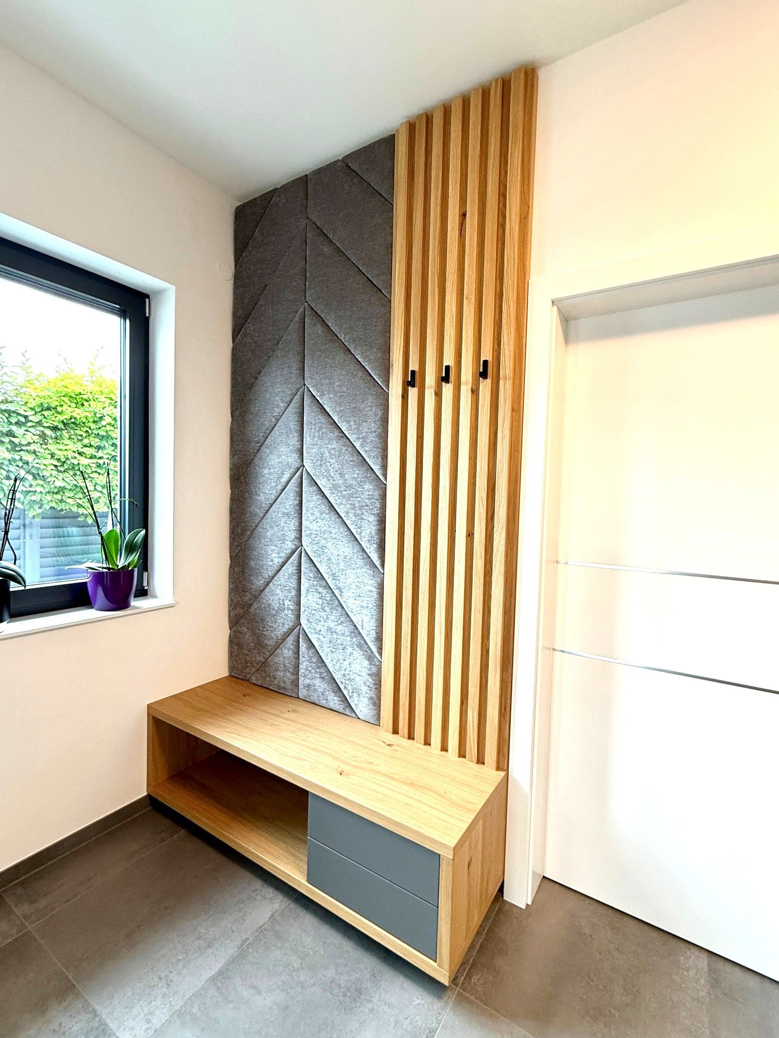 Moderne Eingangsecke mit Holzbank, grauen Schubladen, strukturierter Wandverkleidung und einem Fenster mit Topfpflanze