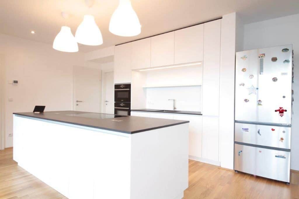 Moderne weiße Küche mit Kochinsel, Pendelleuchten, Einbaubackofen und Edelstahlkühlschrank