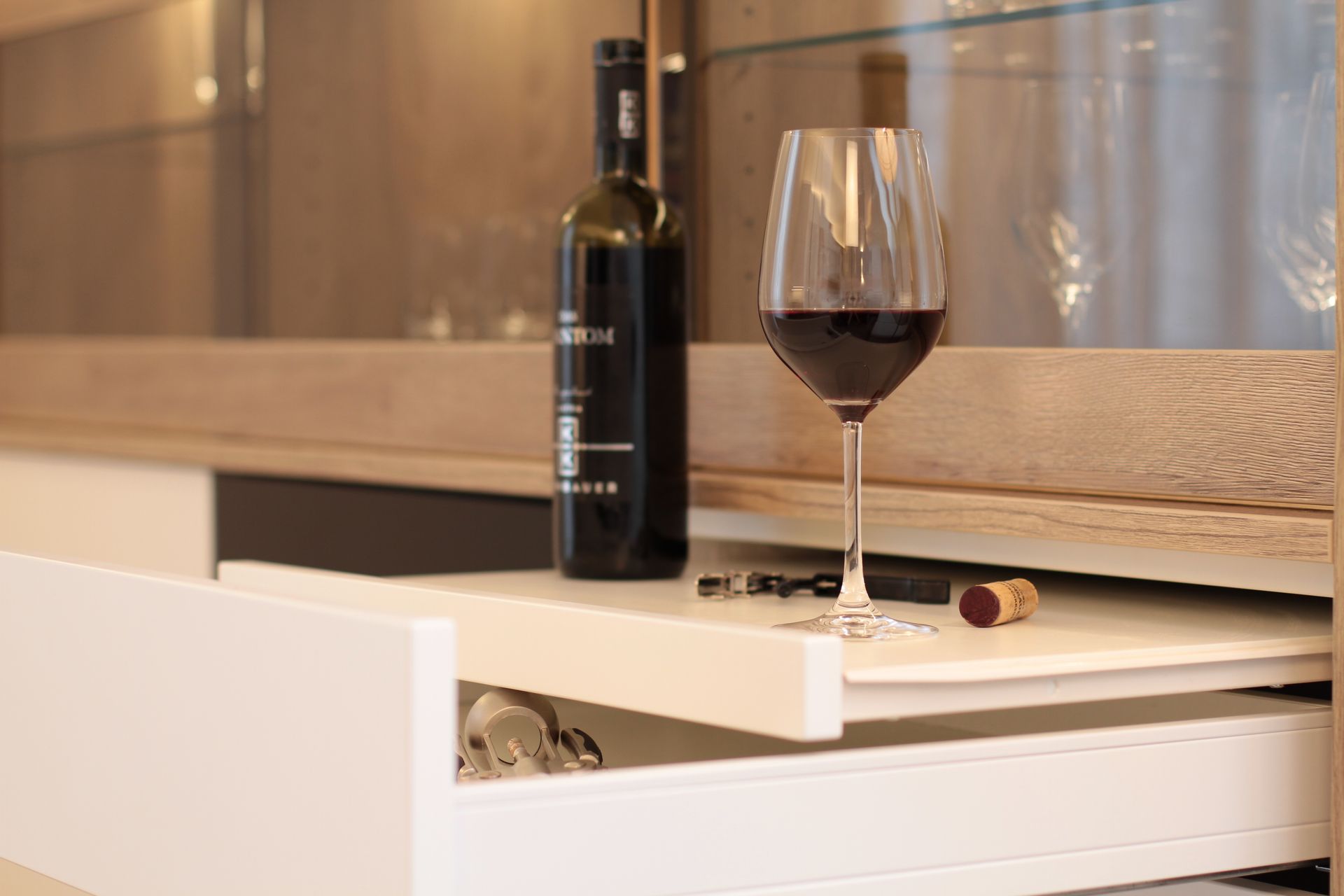 Weinflasche und Glas auf einer weißen Kommode neben einer holzgetäfelten Wand.