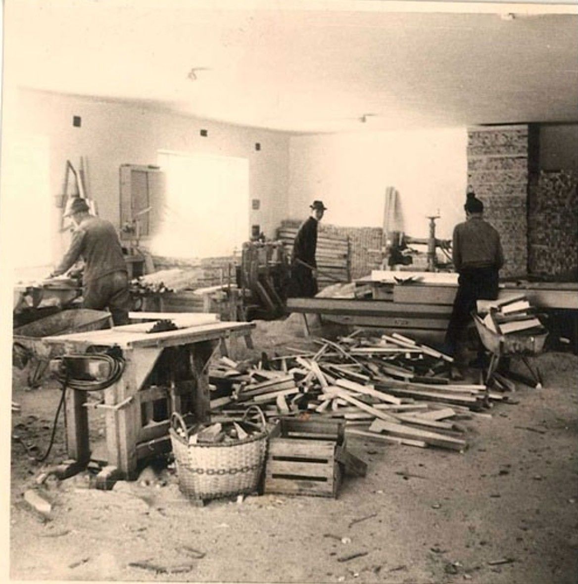 Menschen durchsuchen Trümmer und Holz in einem beschädigten Raum, Werkzeuge und Körbe liegen verstreut herum.