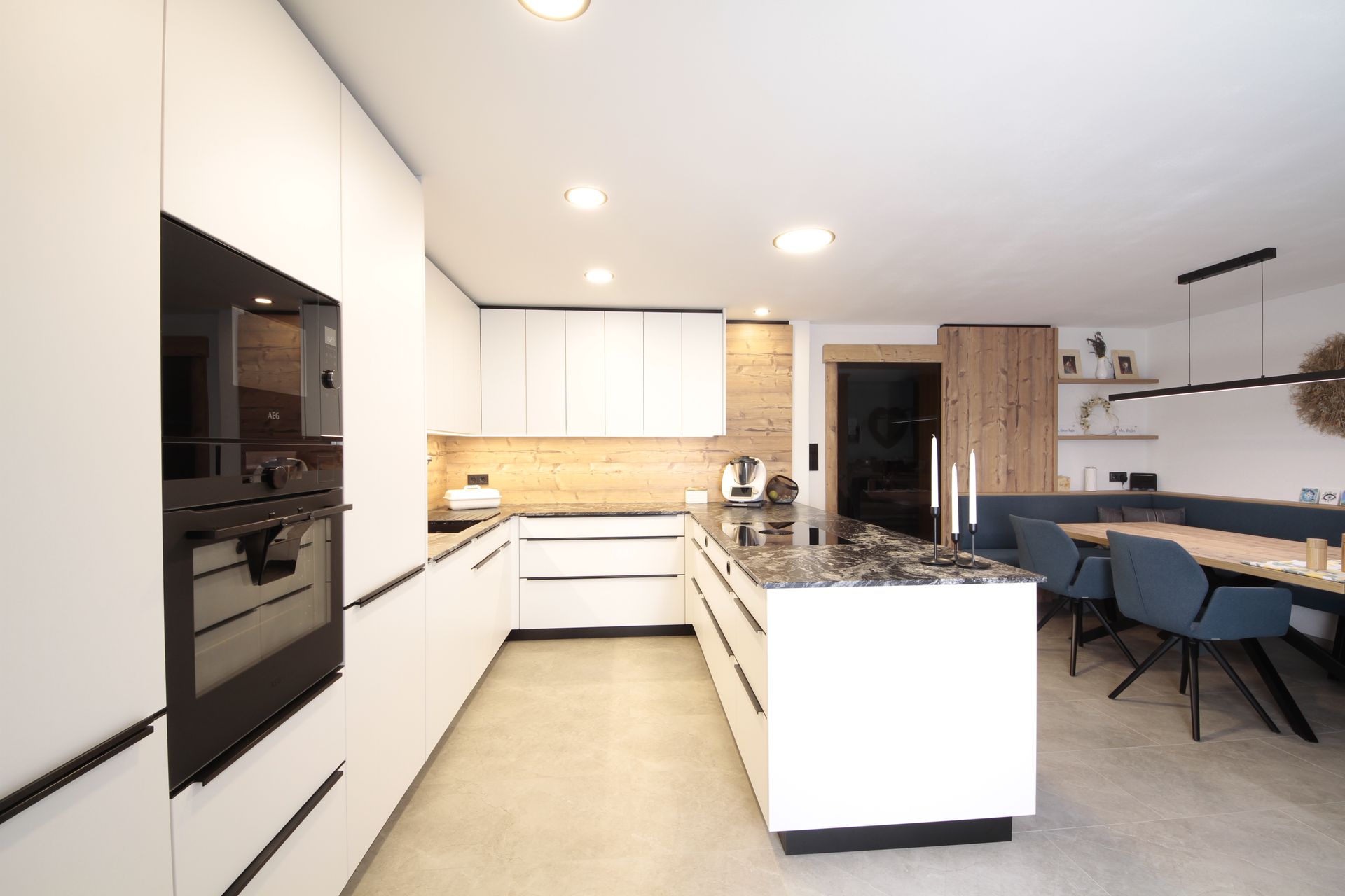 Moderne weiße Küche mit Kochinsel, Einbaubackofen und Esstisch mit blauen Stühlen