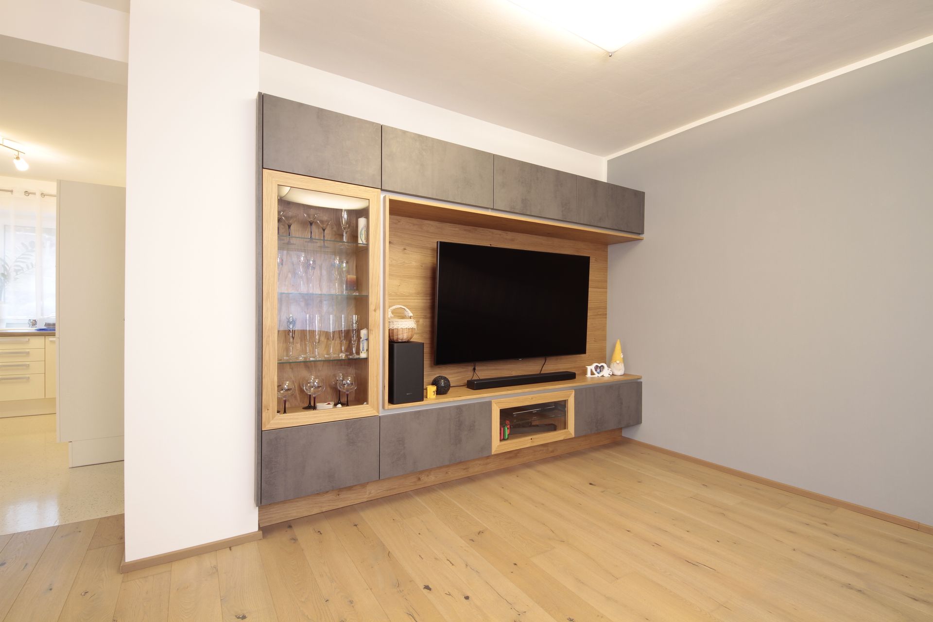 Modernes Wohnzimmer mit hellen Holzböden, grauen Wänden und einer eingebauten TV-Wand mit Schränken.