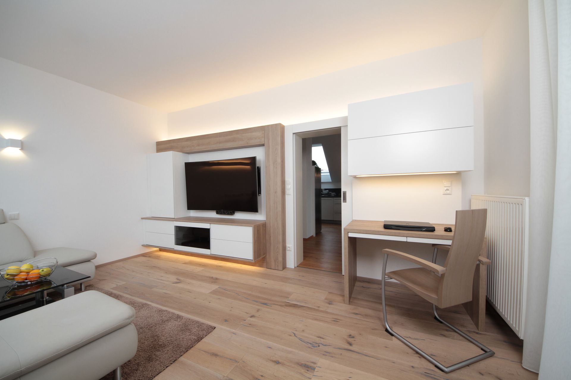 Modernes Wohnzimmer mit wandmontiertem Fernseher, Schreibtischnische, Sofa und hellem Holzboden