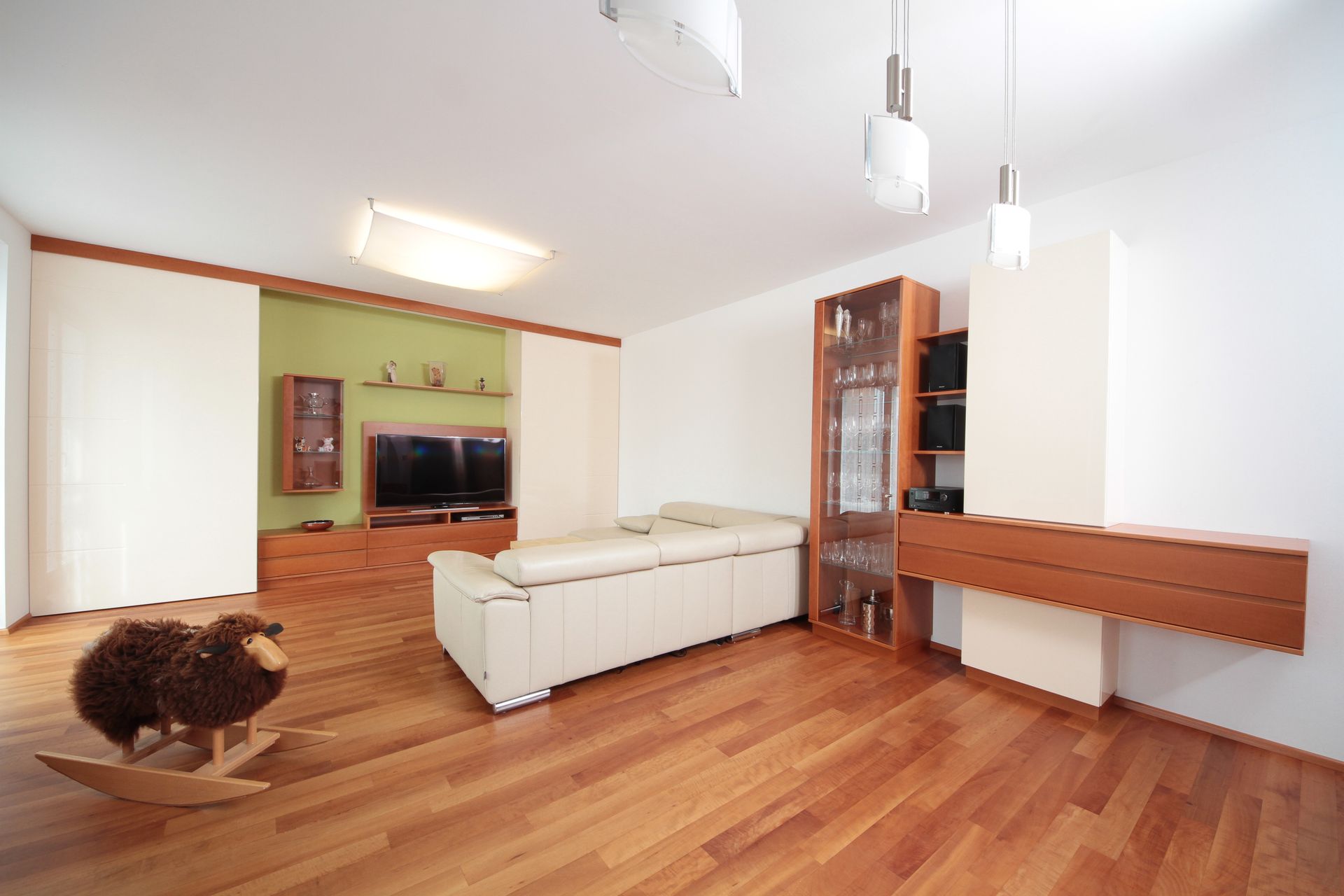 Modernes Wohnzimmer mit Holzboden, weißem Ecksofa, Fernseher, Glasschrank und braunem Sesselteppich.