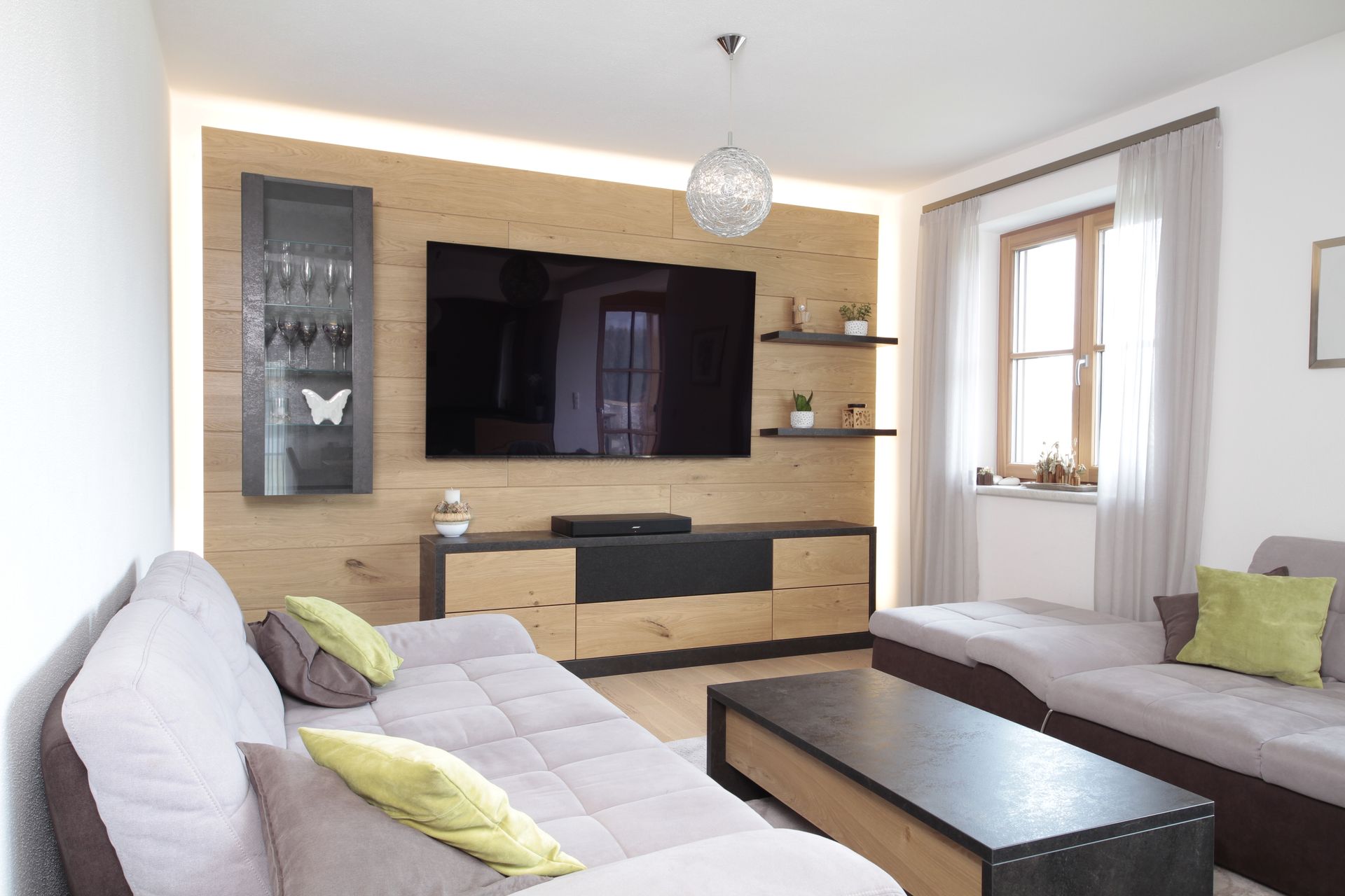 Modernes Wohnzimmer mit zwei Sofas, großem Wandfernseher, Holzkonsole und hellem Sitzbereich am Fenster