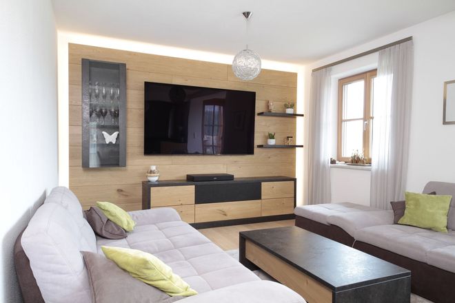 Modernes Wohnzimmer mit zwei Sofas, großem Wandfernseher, Holzkonsole und hellem Sitzbereich am Fenster