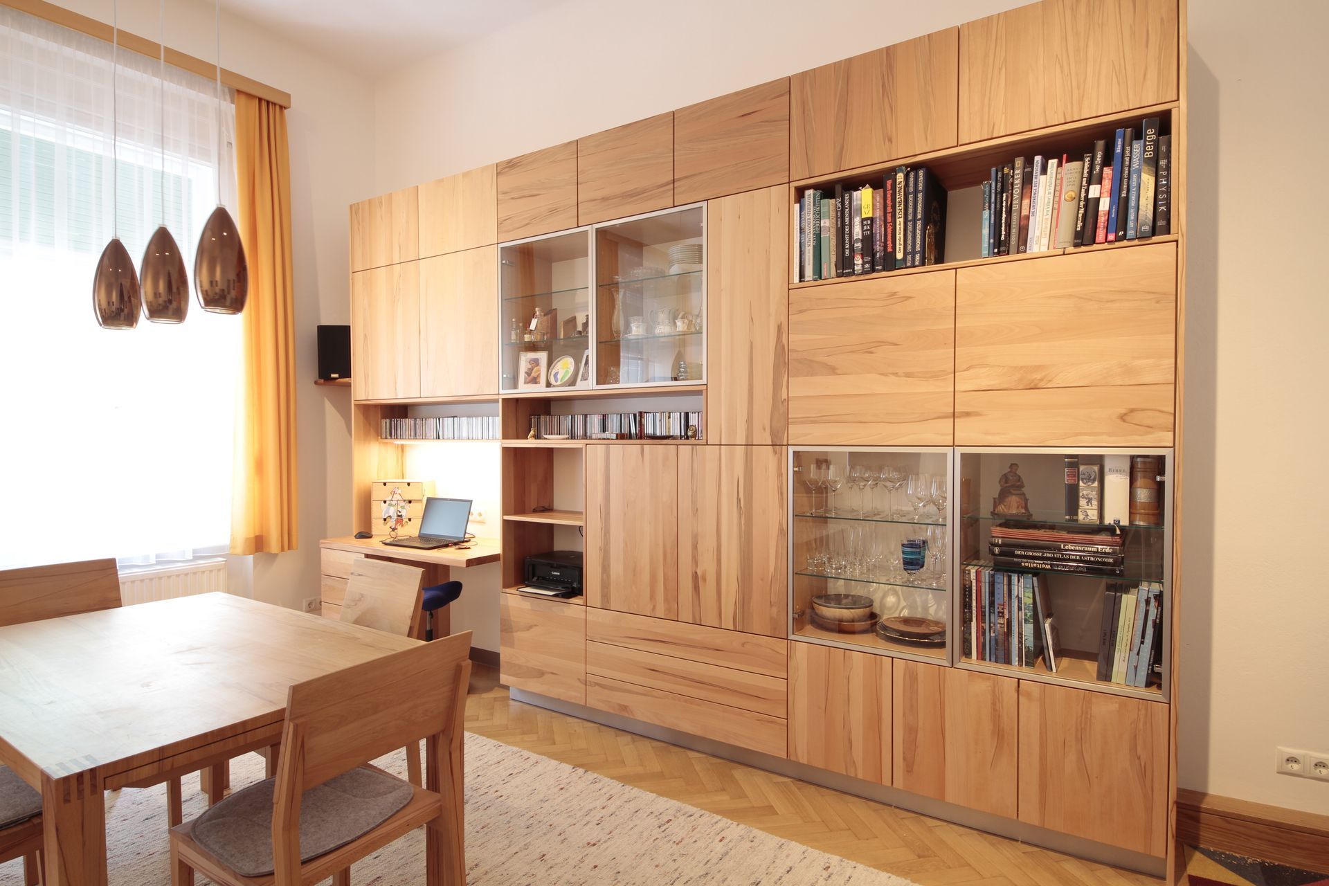 Helles Esszimmer mit hölzernen Wandschränken, Tisch, Stühlen und einem Fenster mit hängender Dekoration