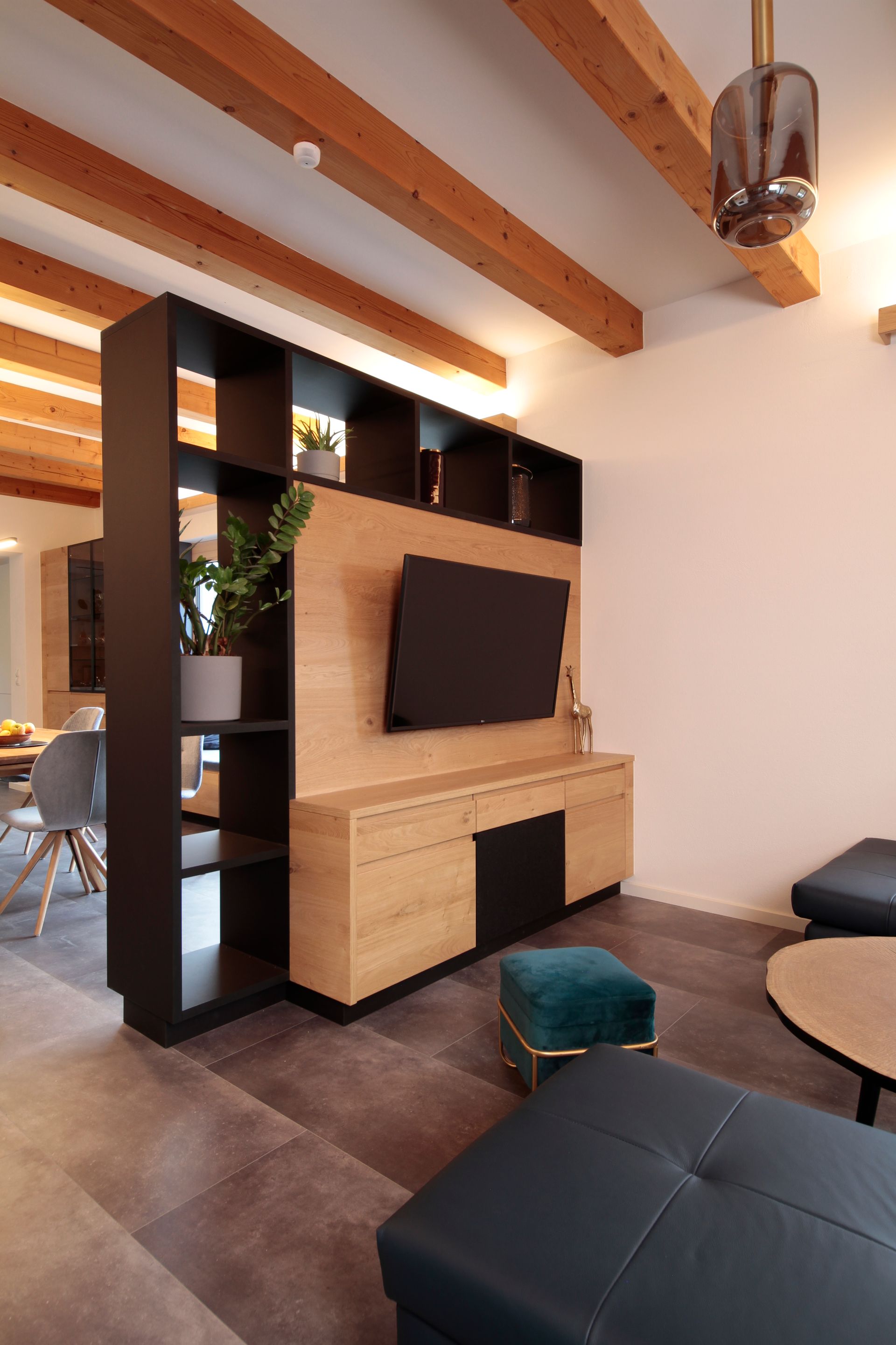 Modernes Wohnzimmer mit Holzbalken, an der Wand montiertem Fernseher, Regalen und dunklen Ledersitzen
