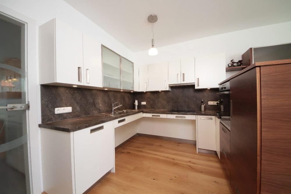 Helle, moderne Küche mit weißen Schränken, dunklen Arbeitsplatten, Holzboden und braunem Kühlschrank
