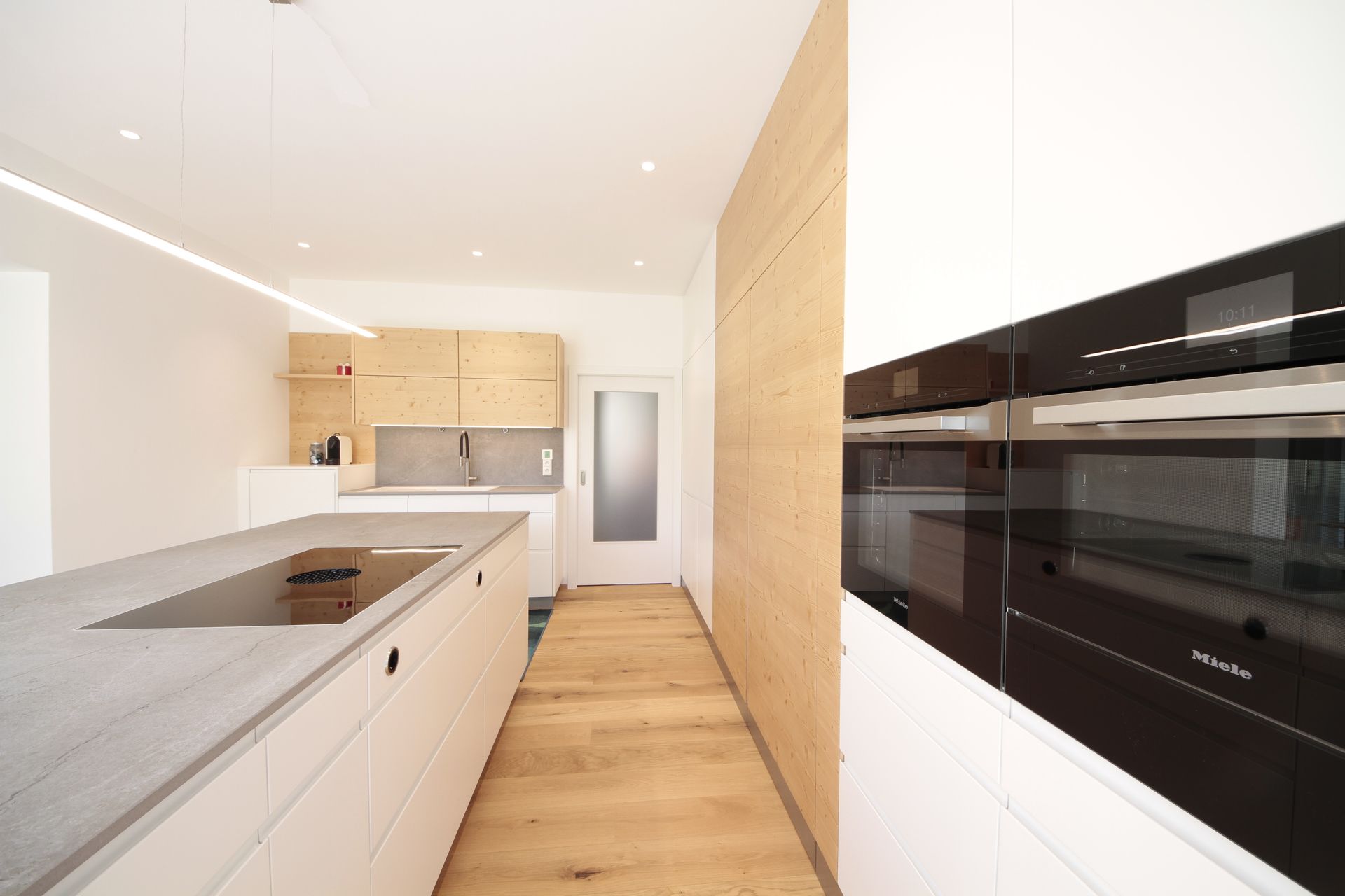 Helle, moderne Küche mit weißen Schränken, Holzelementen und eingebauten schwarzen Backöfen.