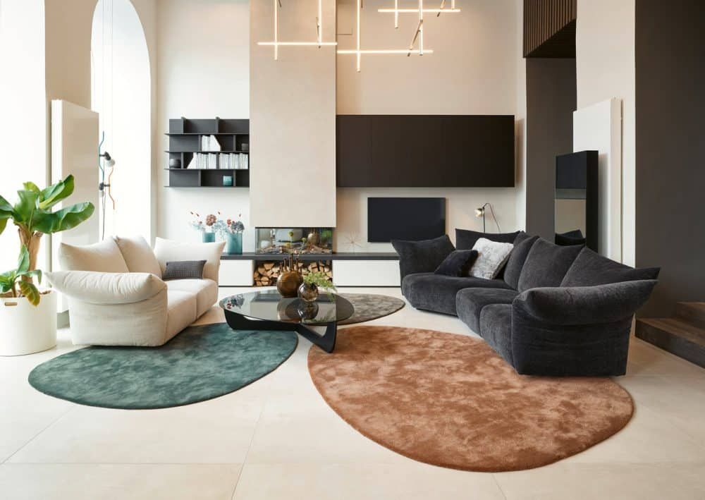Modernes Wohnzimmer mit geschwungenen Sofas, Akzentstühlen, runden Teppichen und einer TV-Wand