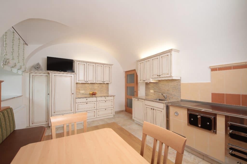Helle, leere Küche mit weißen Schränken, Holztisch, beigefarbenen Fliesen als Spritzschutz und gewölbter Decke