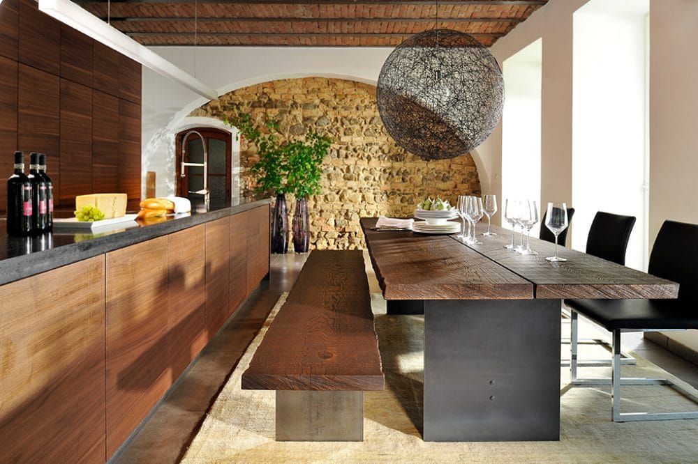 Modernes Esszimmer mit langem Holztisch, Bartheke, Weingläsern und Steinwand.