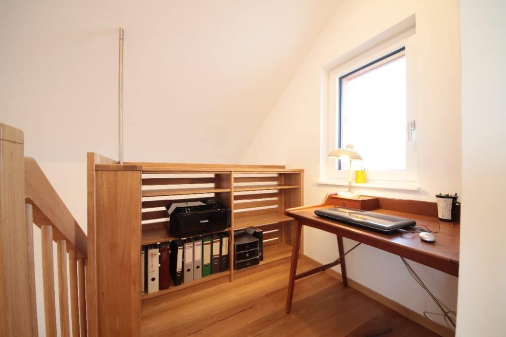 Kleines Dachbodenbüro mit Holzschreibtisch, Regal, Tastatur und einem Fenster, das Licht hereinlässt