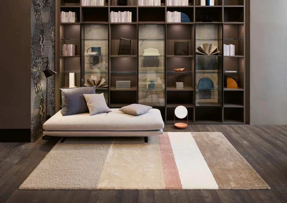 Modernes Wohnzimmer mit beigefarbenem Sofa, großem Holzregal und gestreiftem Teppich in warmen, neutralen Tönen.