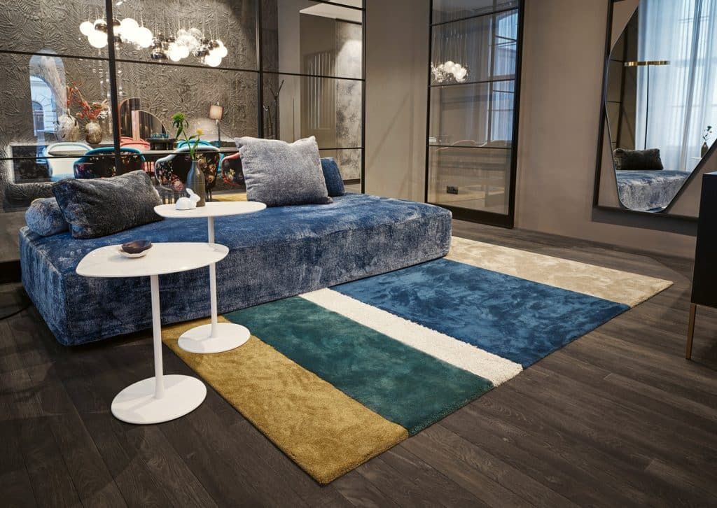 Modernes Wohnzimmer mit blauem Sofa, weißem Beistelltisch und farbenfroh gestreiftem Teppich.
