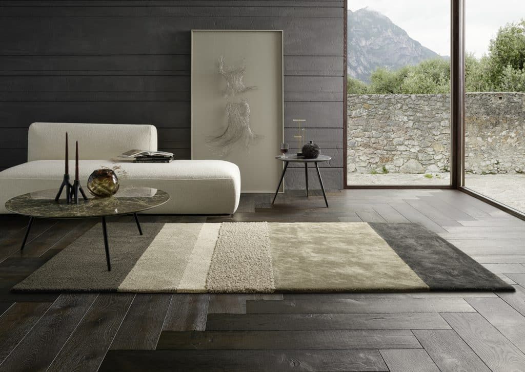 Modernes Wohnzimmer mit niedrigem Sofa, dunklem Holzboden, großem Teppich und Bergblick durch ein bodentiefes Fenster