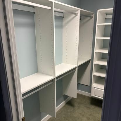 Walk-in closet with white shelving and hanging rods in a small carpeted room