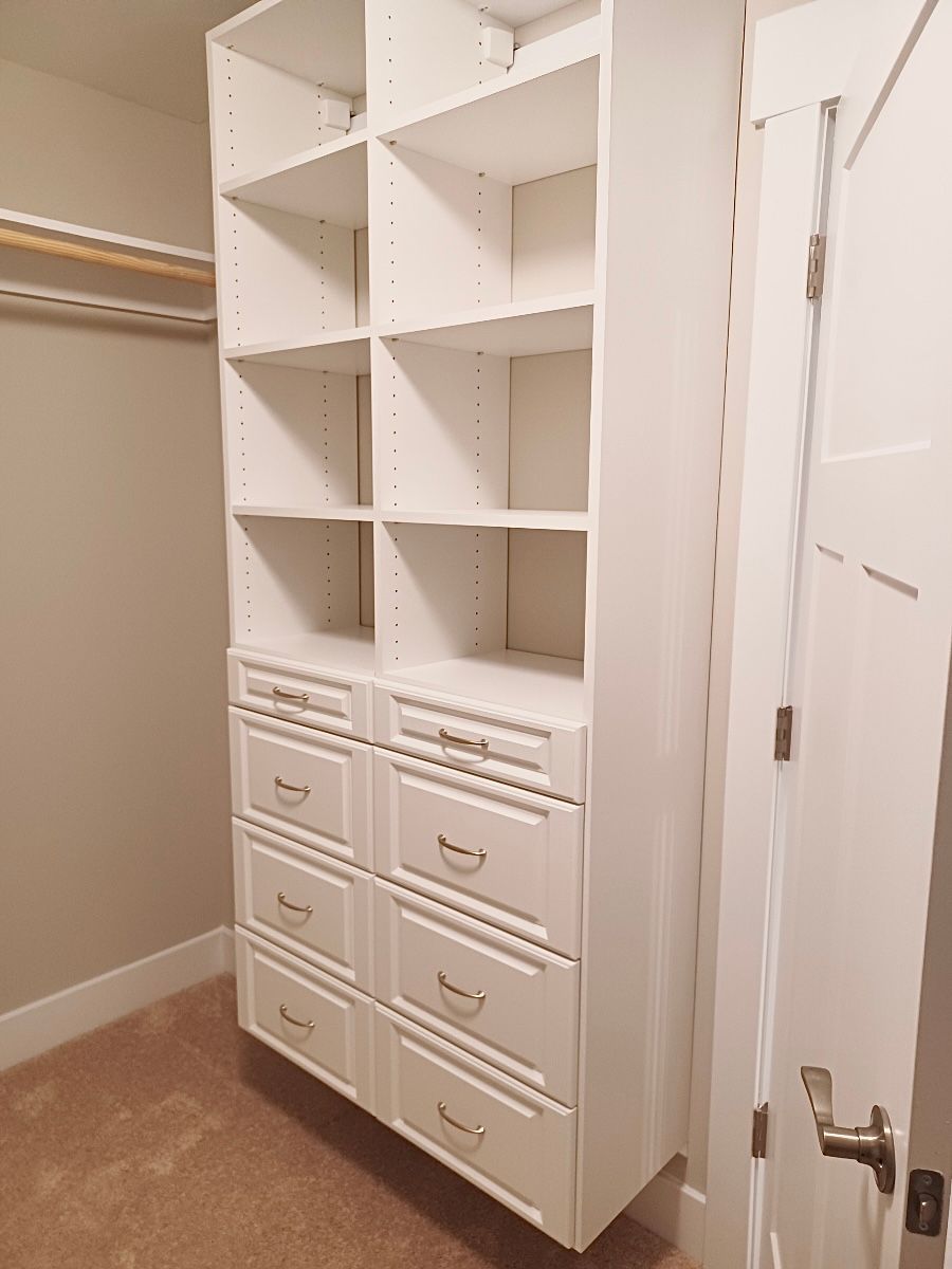 White built-in closet organizer with shelves and drawers in a beige carpeted room