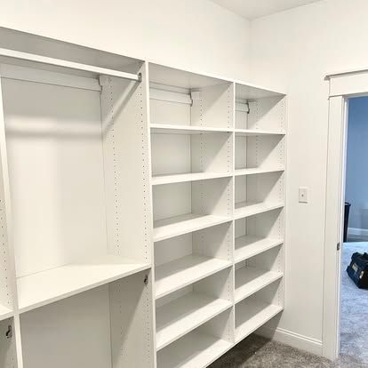 White built-in closet with open shelves and hanging rod in a bright room.