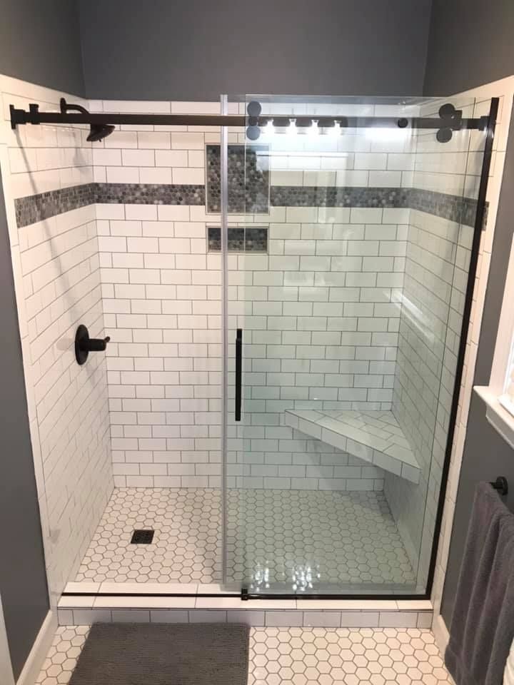 Glass walk-in shower with white subway tile, black fixtures, and a built-in corner bench.