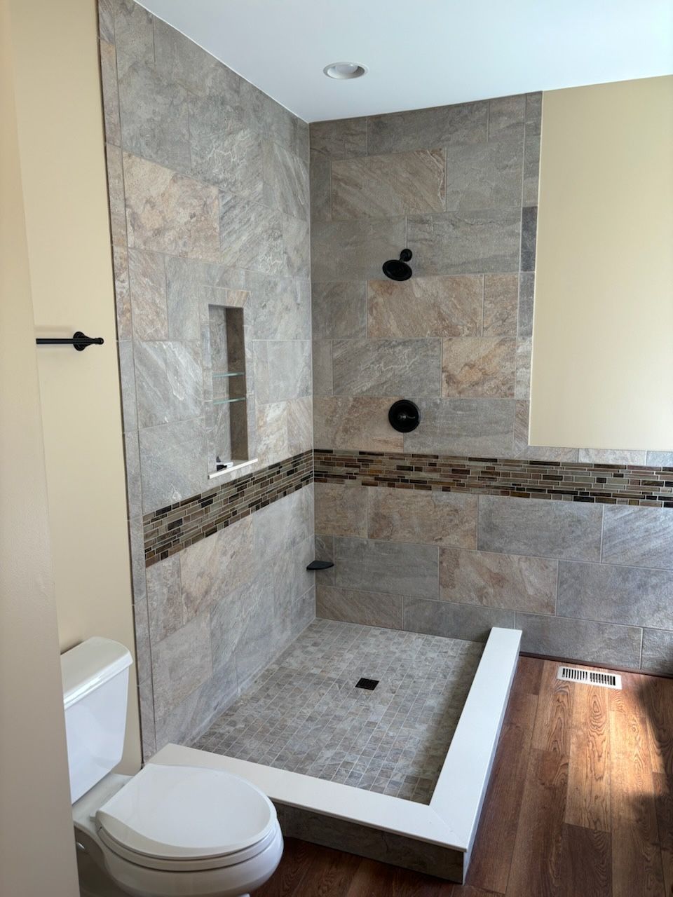 Modern tiled walk-in shower with bench, built-in niche, and toilet beside it.