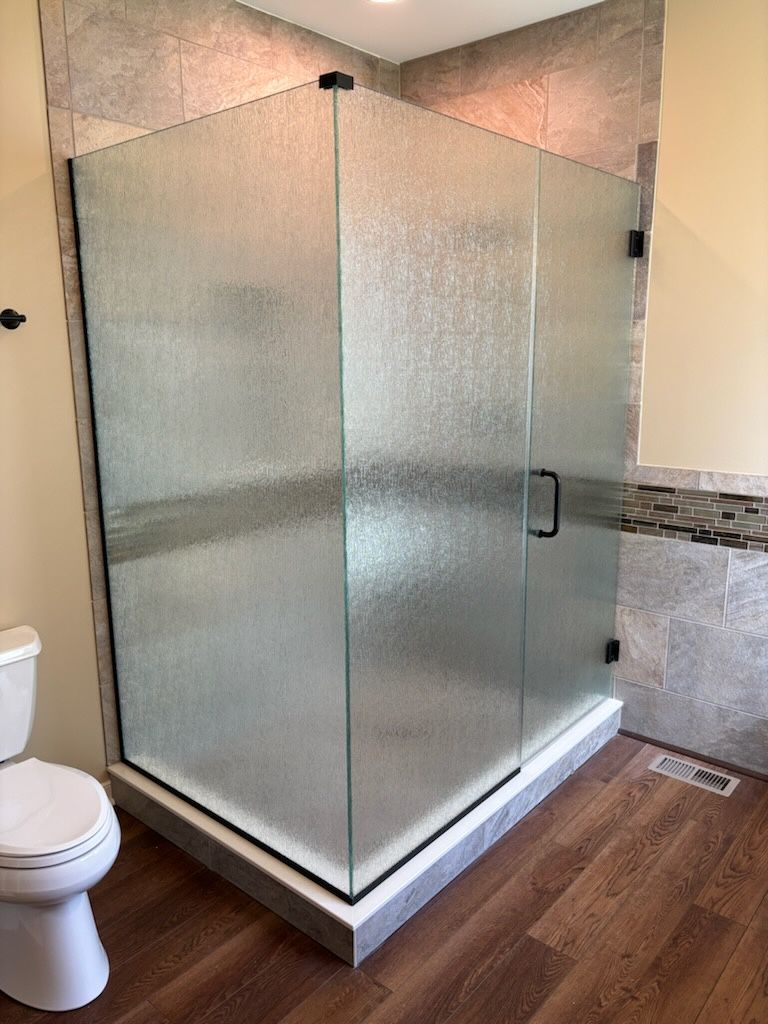 Glass corner shower enclosure in a bathroom with wood-look floor and toilet nearby