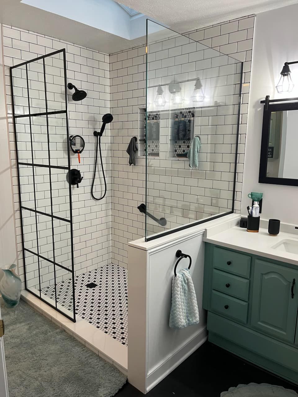 Modern bathroom with glass shower, black fixtures, white tile, and green vanity beside a mirror