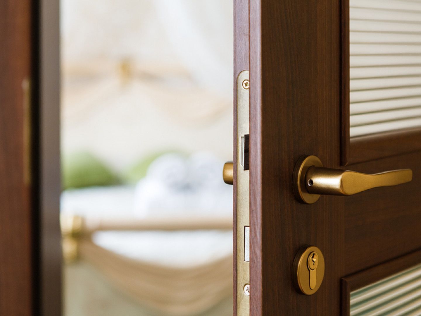Open wooden door with brass handle, showing a blurred bedroom beyond