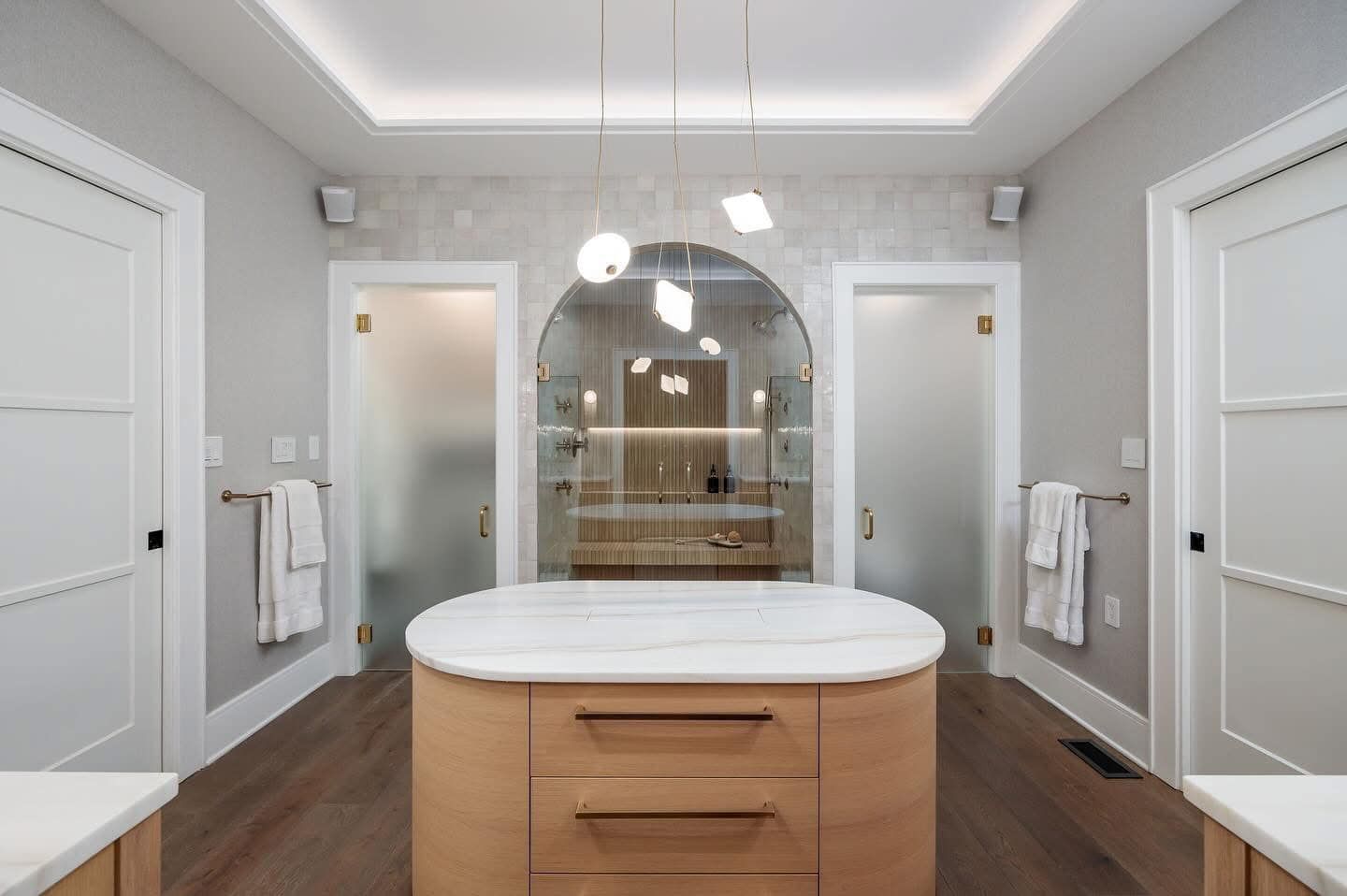 Modern bathroom with double doors, twin frosted showers, and a central vanity under a large mirror.