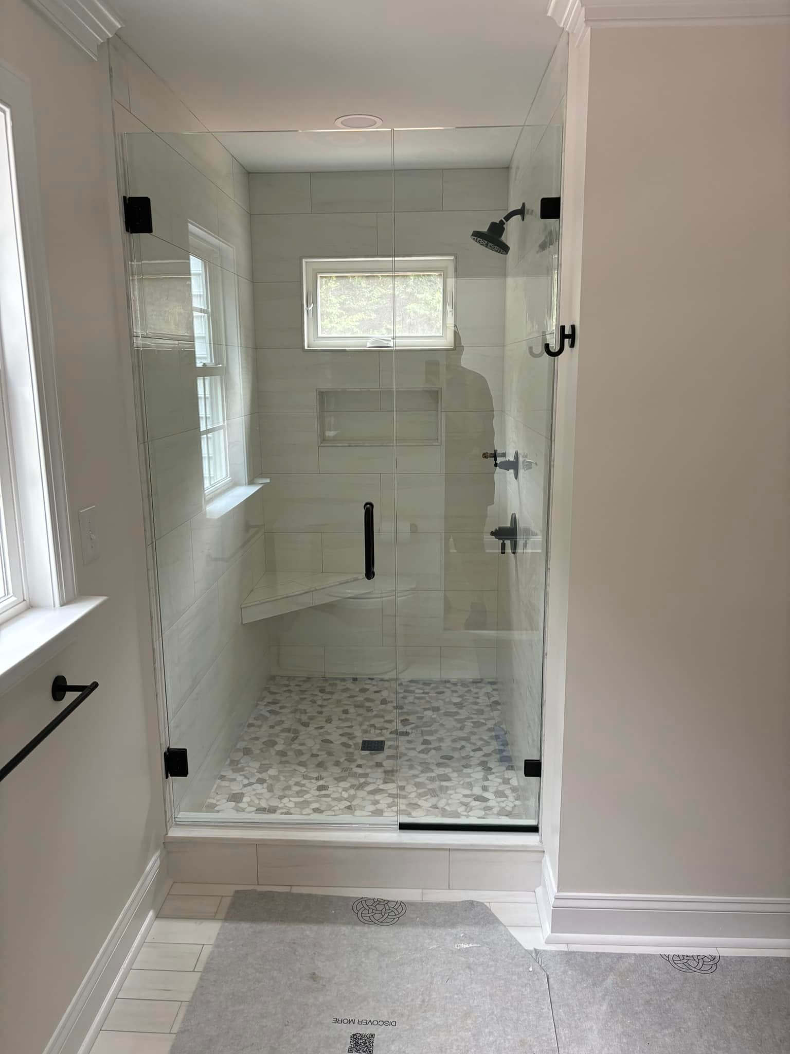 Small white-tiled shower with glass door and patterned shower floor in a bright bathroom.