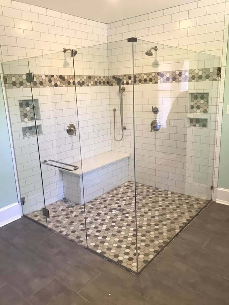 Glass-enclosed walk-in shower with white tile walls and mosaic floor in a bathroom