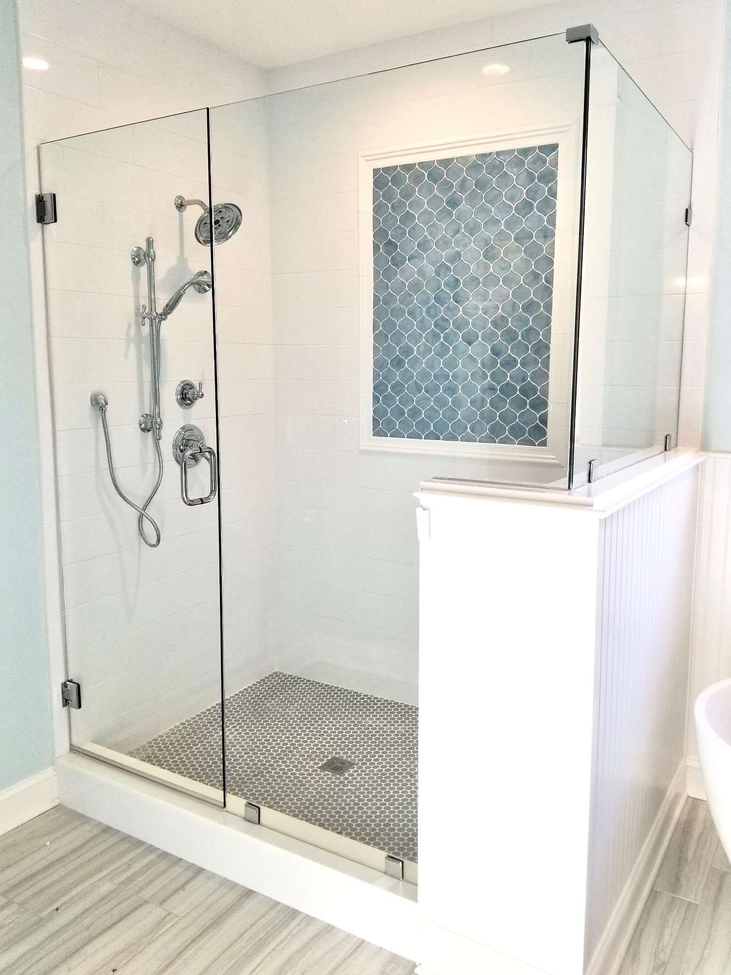 Glass walk-in shower with chrome fixtures, pebble floor, and frosted window in a bright bathroom