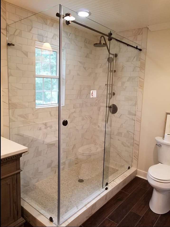 Glass-enclosed walk-in shower with beige tile, rain showerhead, and partial toilet visible beside it