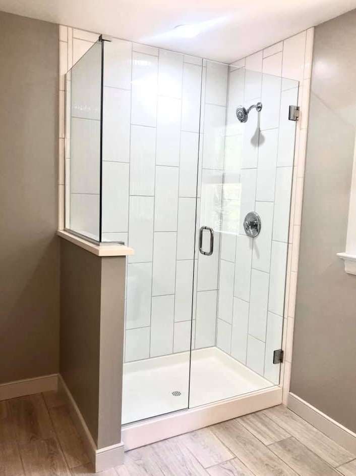 Glass corner shower enclosure with white tile walls and chrome fixtures in a modern bathroom