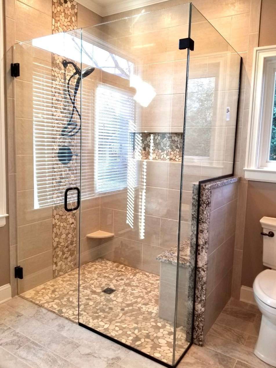 Glass walk-in shower with pebble floor and beige tile in a bathroom