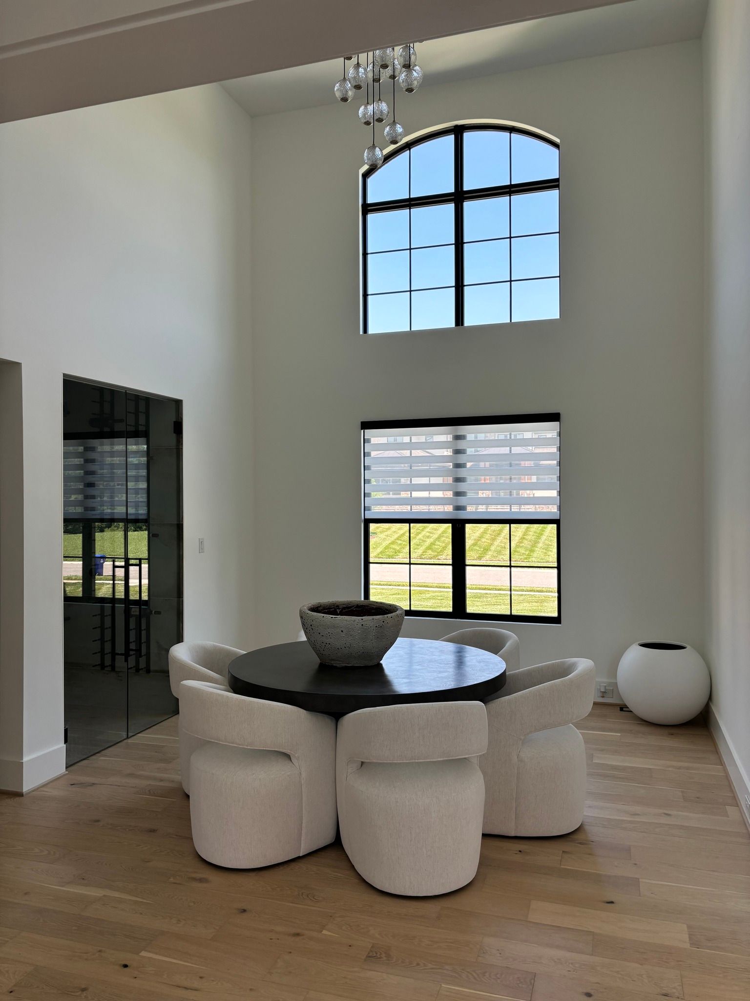Bright modern dining area with round table, cream stools, large arched window, and wood floors.